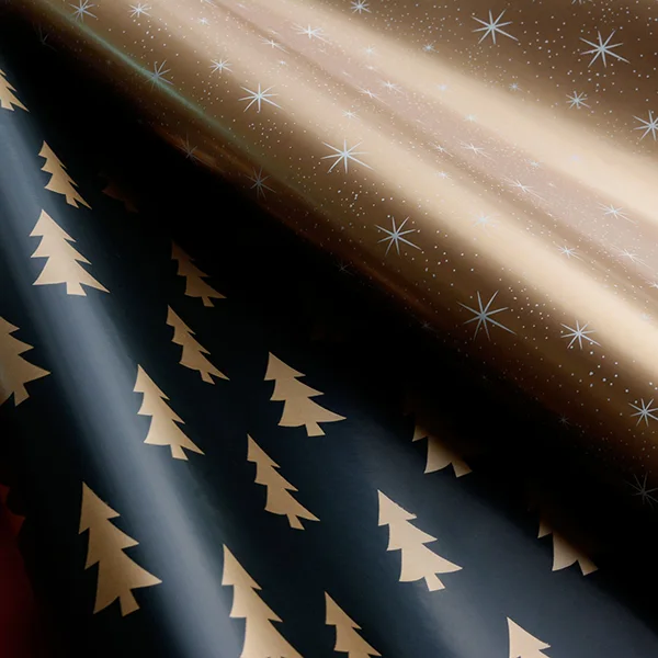 2 rolls of wrapping paper fanned out to show designs of a gold tree with black background and white stars with a gold background.