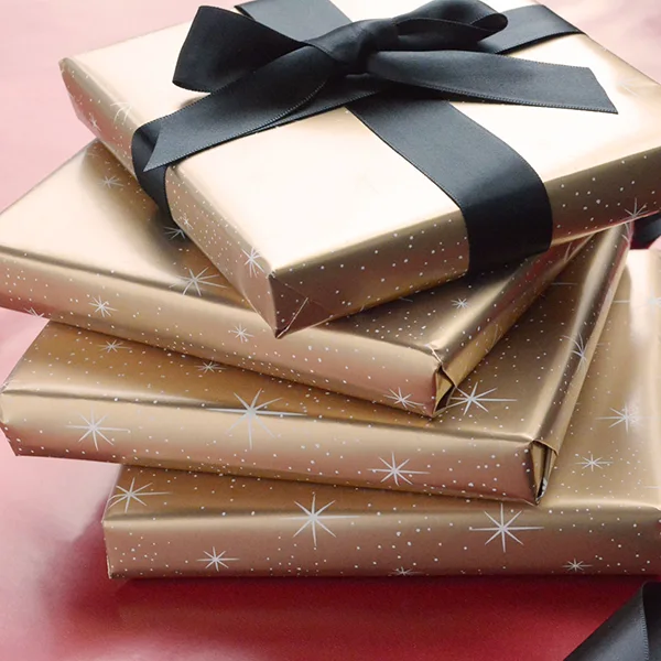 4 stacked slimline boxes, each wrapped in the same metallic gold with white stars wrapping paper. One box finished with a black satin ribbon.