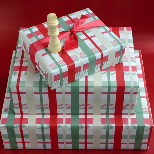 3 stacked boxes wrapped in a check design in red, grey and sage. A chess piece sits atop the first box.