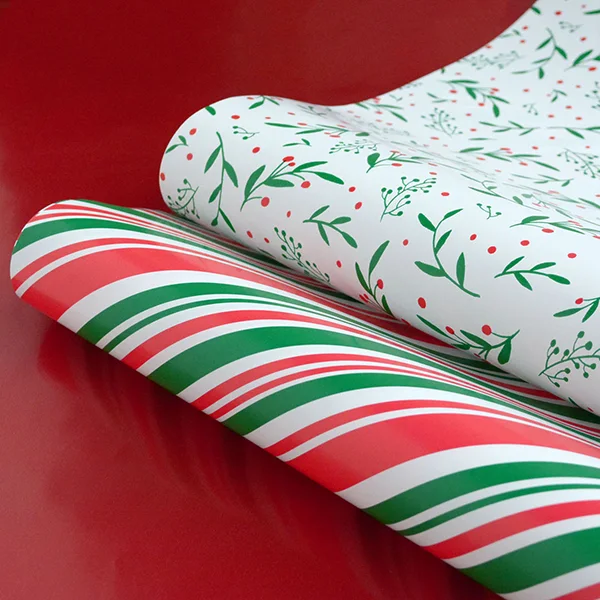 2 rolls of wrapping paper unrolled slightly to show a candy cane and a holly design, both in red and green.